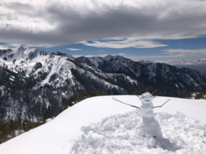 Snowman on snowy mountaintop facing other snow-covered mountains